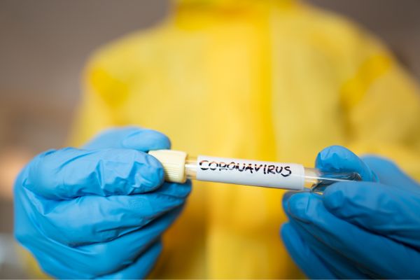 Gloved hands holding a vial labeled with Coronavirus.